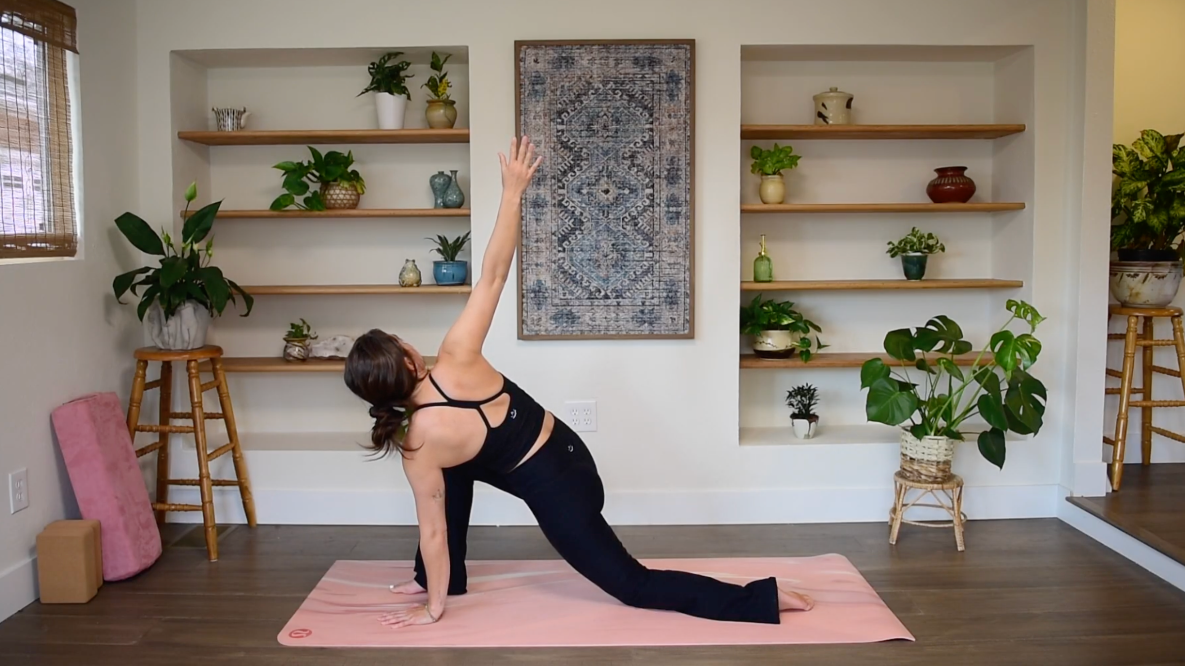 Caitlin K'eli in a low lunge with back knee down, planting one hand on the mat and reaching the opposite arm overhead in Revolved Low Lunge.